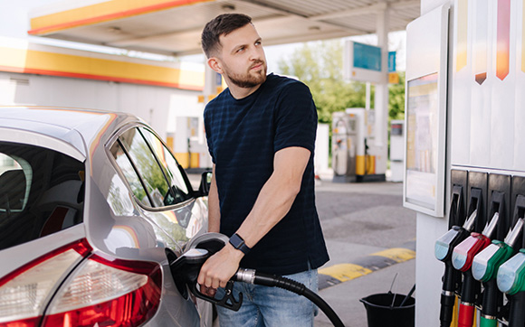 man refuelling car at a gas station and looking at pumps