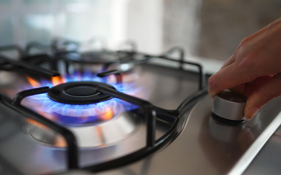 Close up of a person adjusting the temperature on a gas range with the flame visable